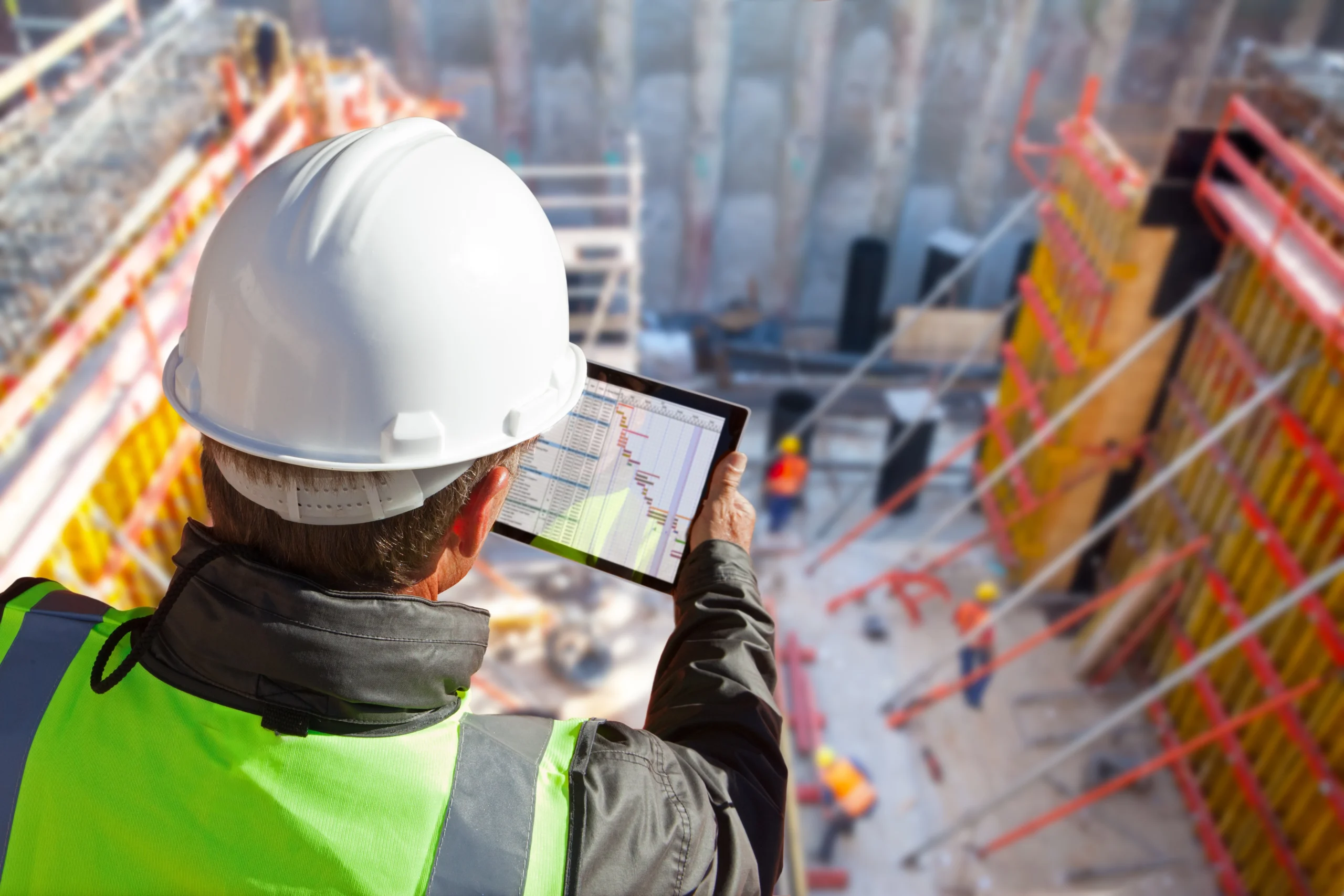 civil engineer or architect with hardhat on construction site checking schedule on tablet computer