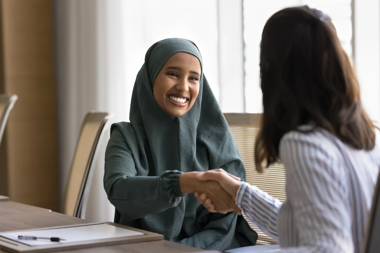 Happy beautiful Arab business professional woman in abaya shaking hands with European female colleague after negotiation, smiling, thanking for consultation, deal, partnership, meeting